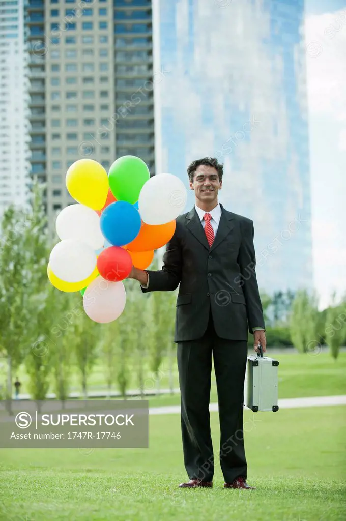 Smiling businessman holding bunch of balloons