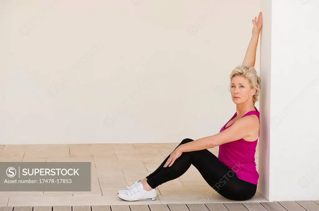 Mature woman sitting against wall, stretching arm