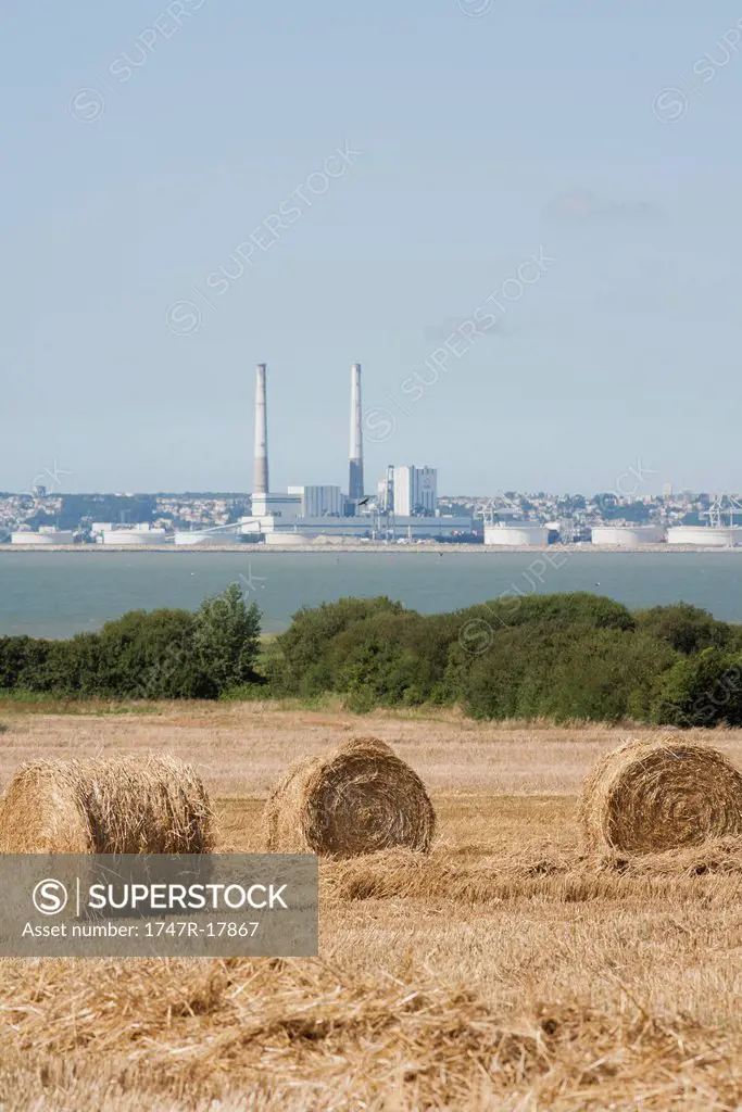 Field with bales of hay in foreground, power station in background