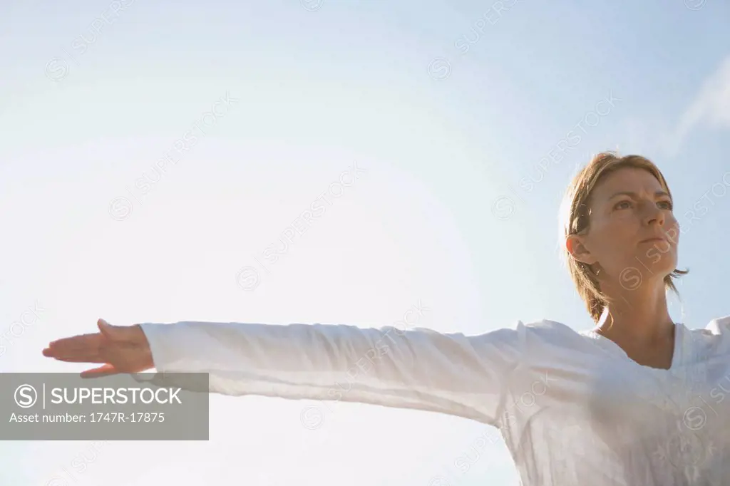 Mid_adult woman with arms outstretched outdoors, low angle view