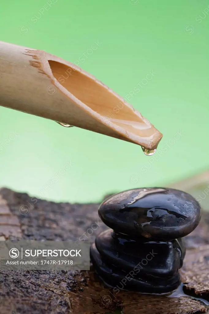 Water droplet hanging off bamboo spout over stack of pebbles