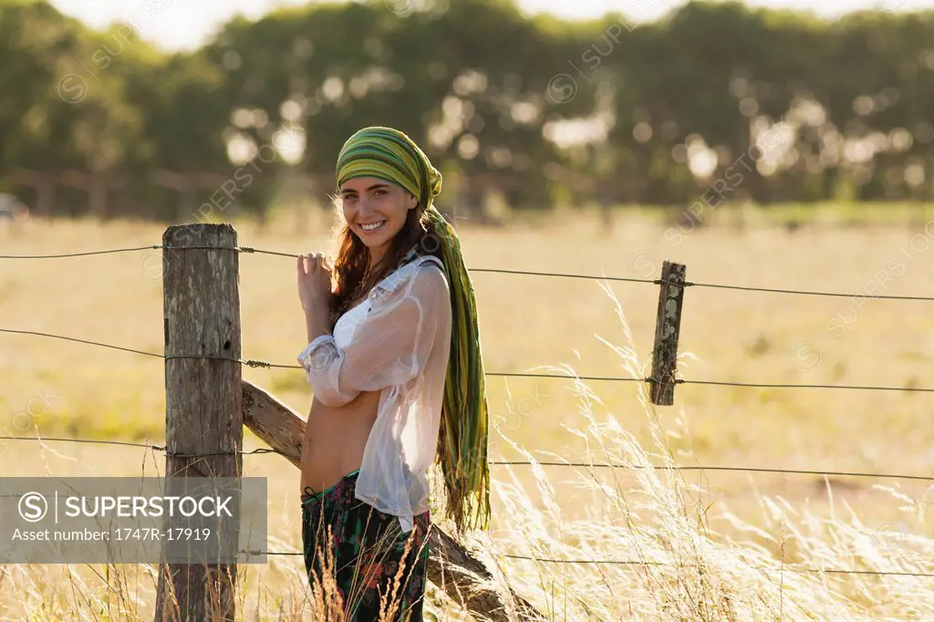 Young hippie woman standing by fence in field