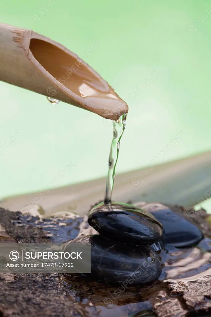 Bamboo spout pouring water over stack of black pebbles
