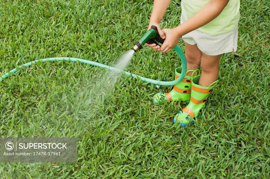 Girl watering lawn with garden hose, cropped