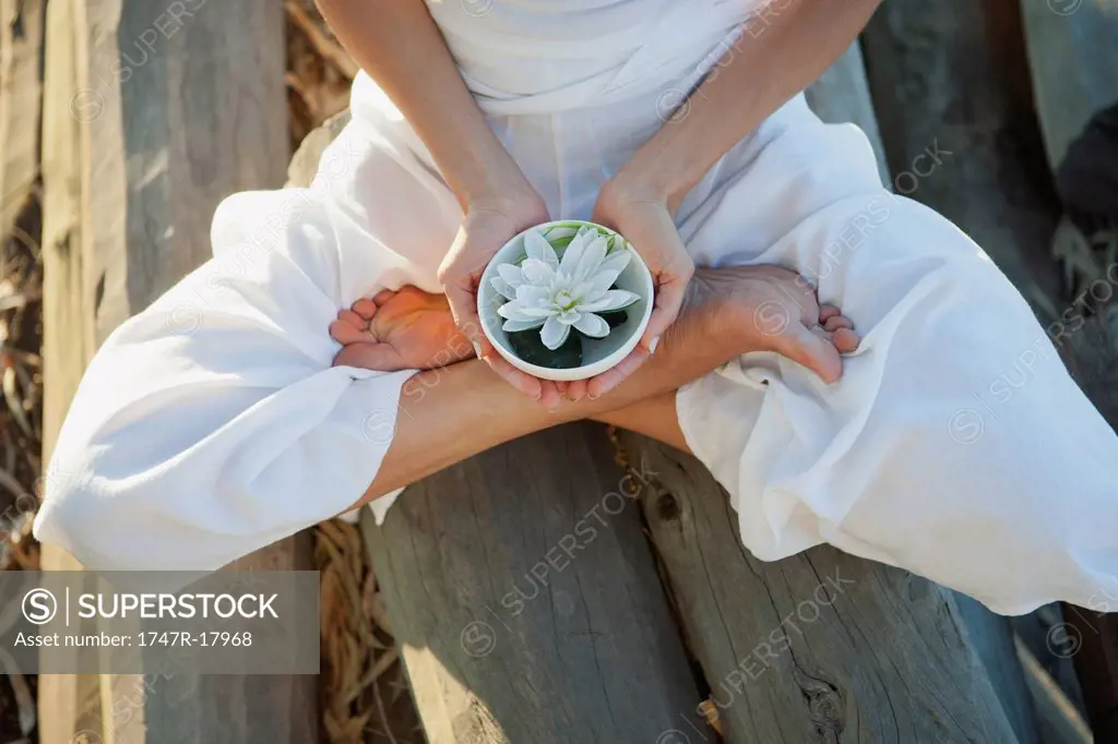Woman sitting in lotus position, holding water lily in bowl