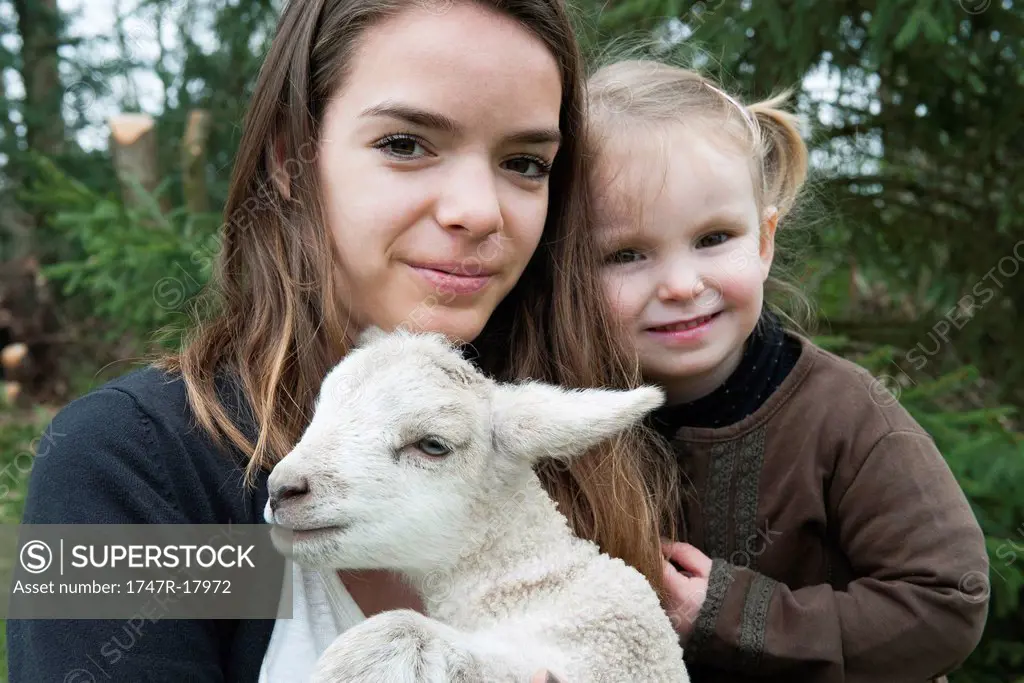 Teenage girl and little sister with pet lamb, portrait