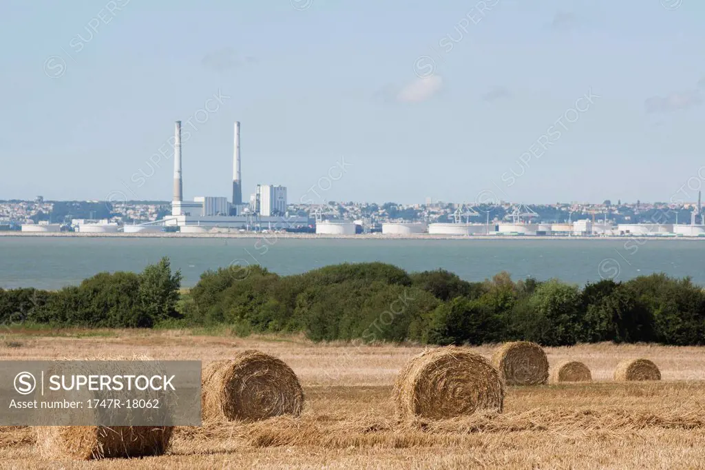 Field with bales of hay in foreground, power station in background