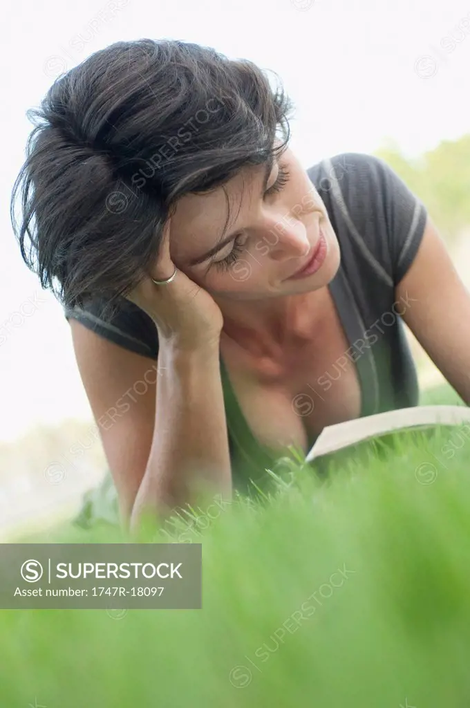 Woman lying on grass reading book