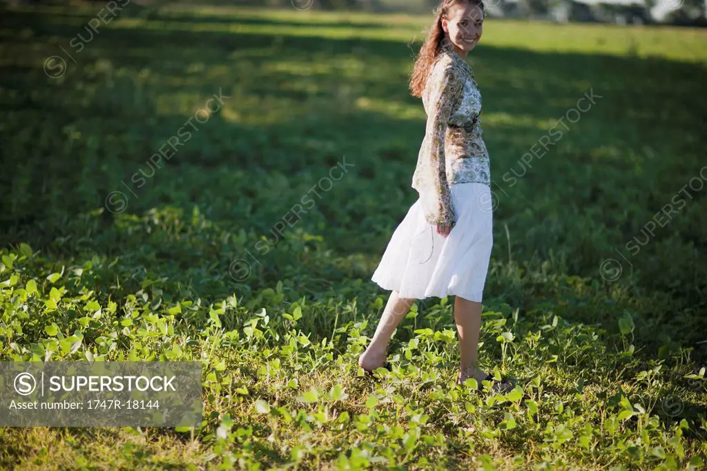 Young woman walking in field, looking over shoulder at camera