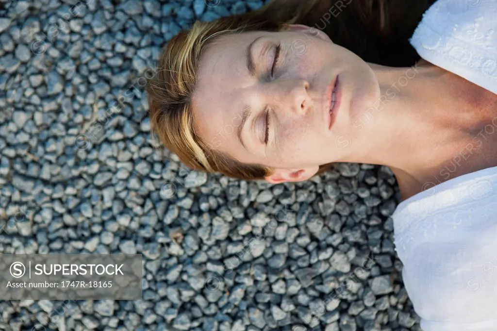 Mid_adult woman lying on gravel with eyes closed, cropped