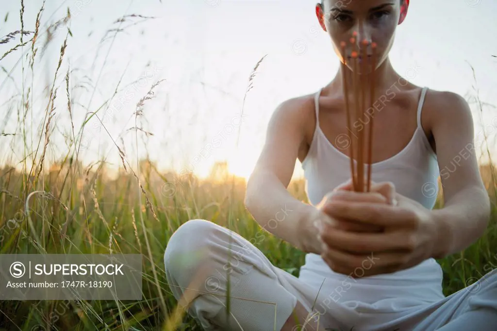 Young woman sitting in grass, holding incense sticks