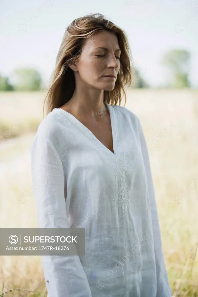 Mid_adult woman in tunic standing outdoors with eyes closed