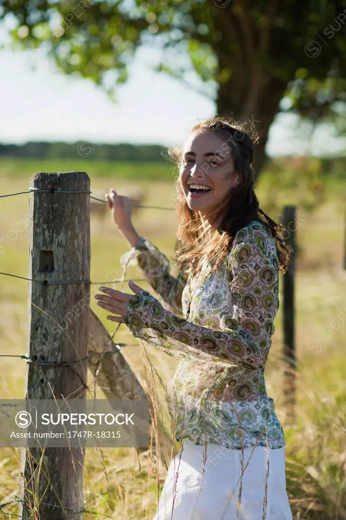 Young woman standing by fence in field