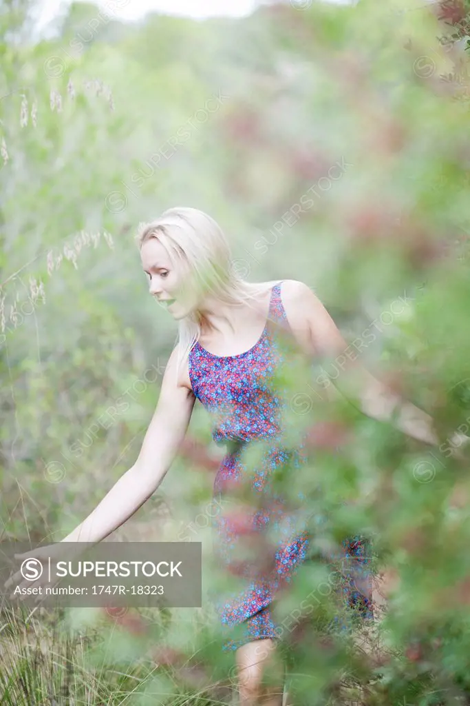 Young woman walking in nature, touching tall grass