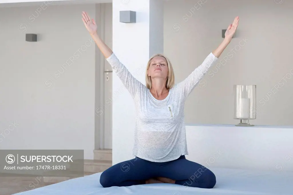 Young woman exercising on bed with arms raised