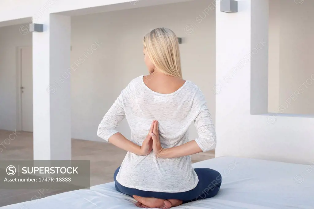 Woman doing reverse prayer position on bed, rear view