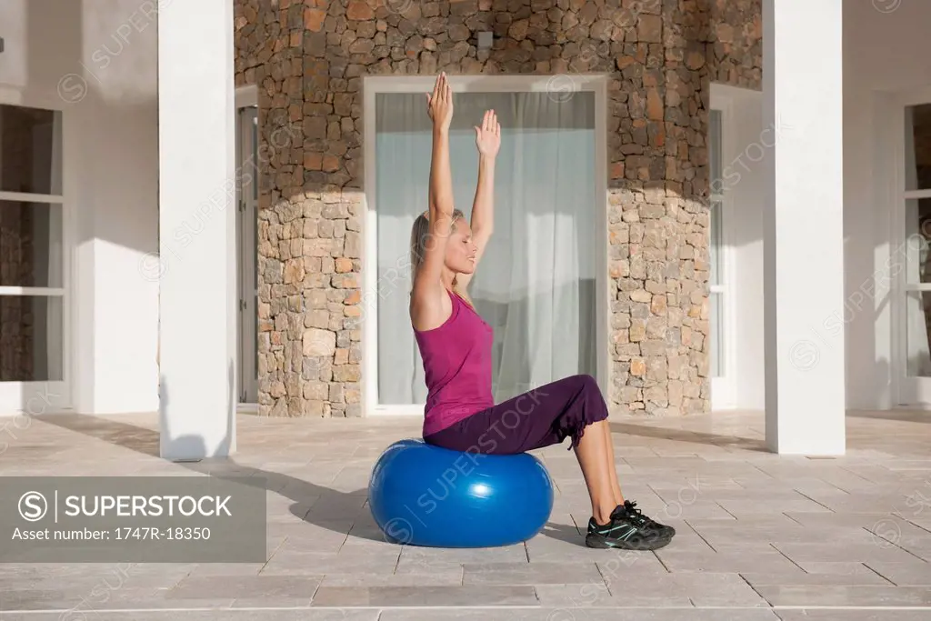 Young woman doing exercise on fitness ball with eyes closed