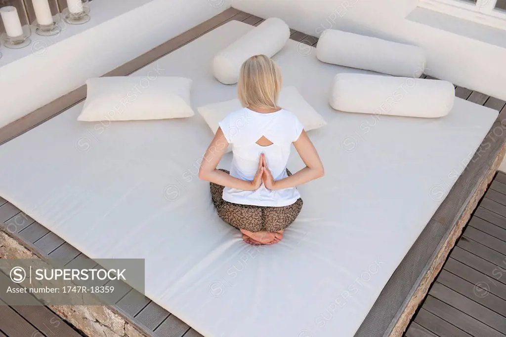 Woman doing reverse prayer pose on bed in patio, rear view