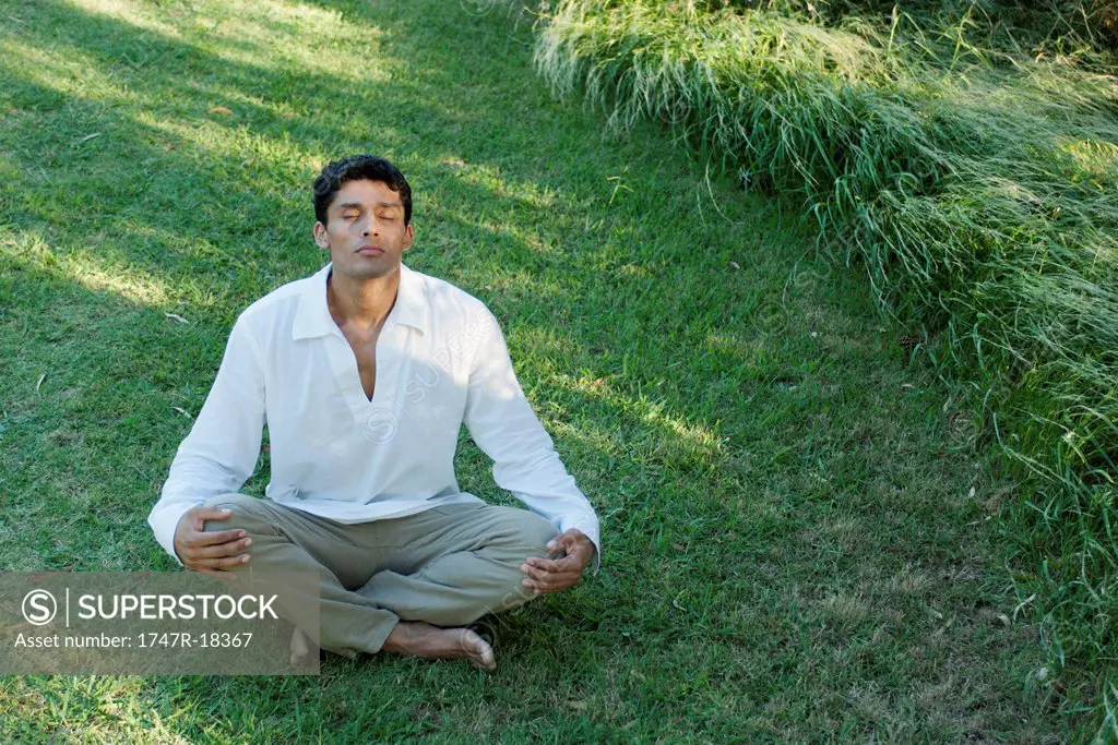 Mid_adult man meditating on grass