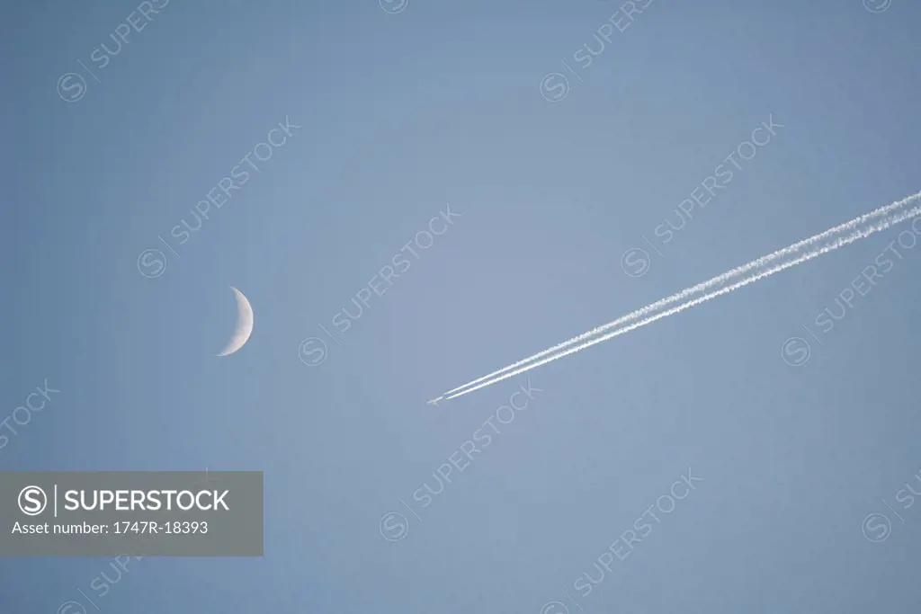 Vapor trail and crescent moon in sky