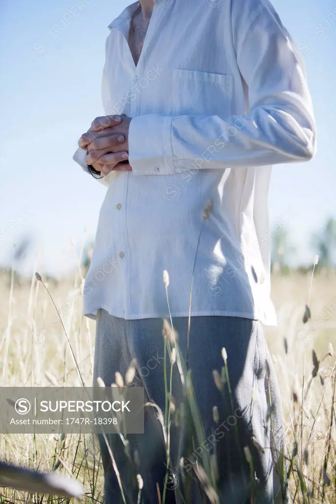Man meditating in field, cropped