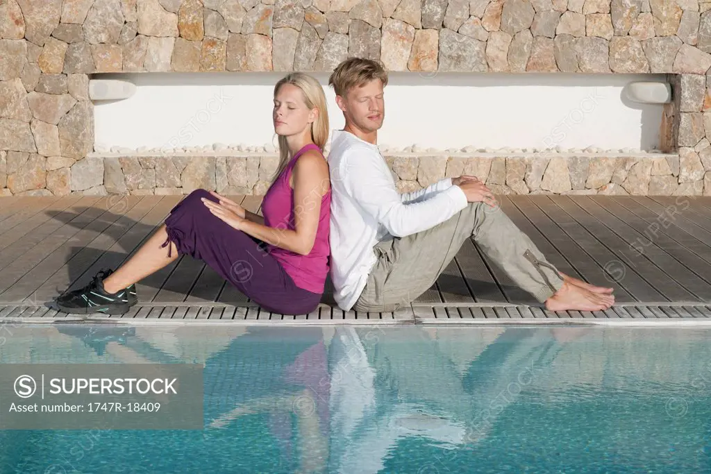 Young couple sitting back to back at poolside