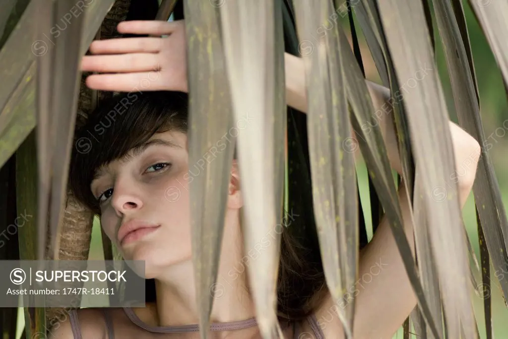 Young woman behind tropical foliage, portrait