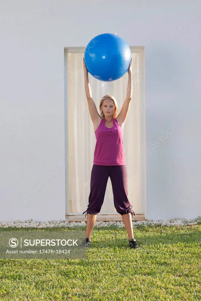 Young woman holding up fitness ball above head