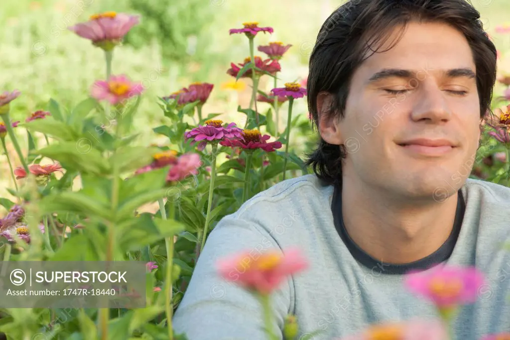 Mid_adult man in zinnia flowers with eyes closed, smiling