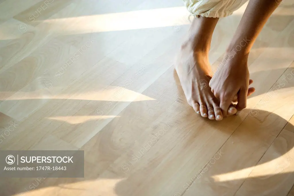 Woman bending forward touching big toe, low section, cropped