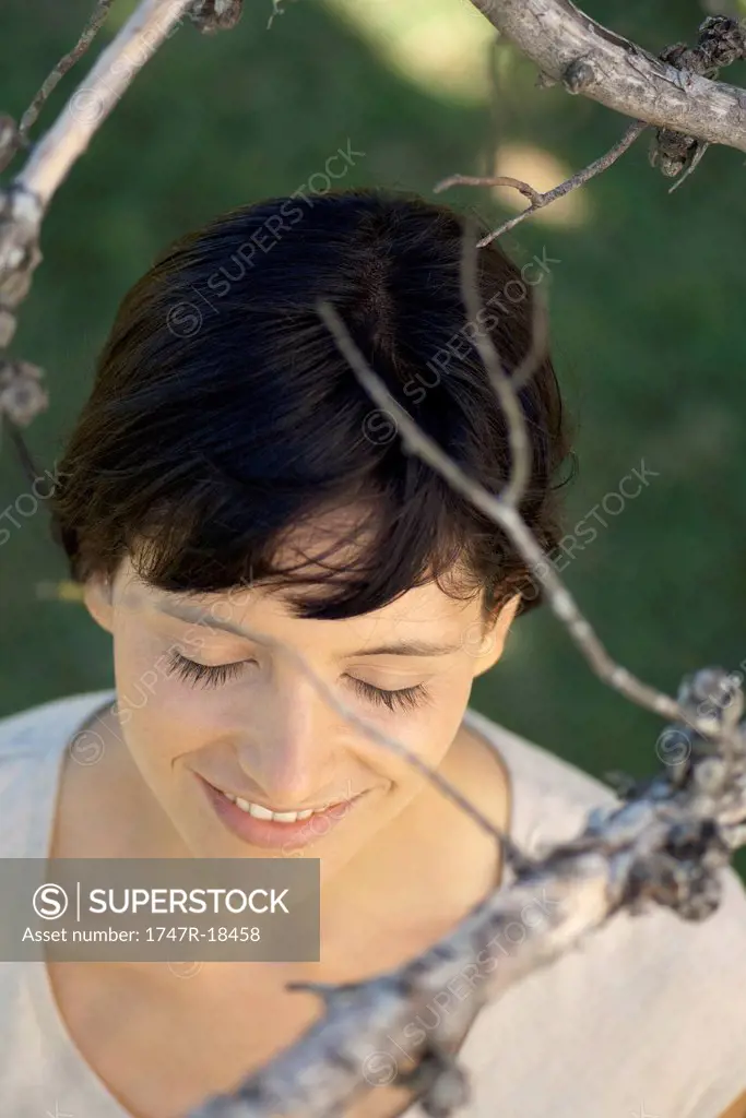 Woman under tree branches with eyes closed, smiling