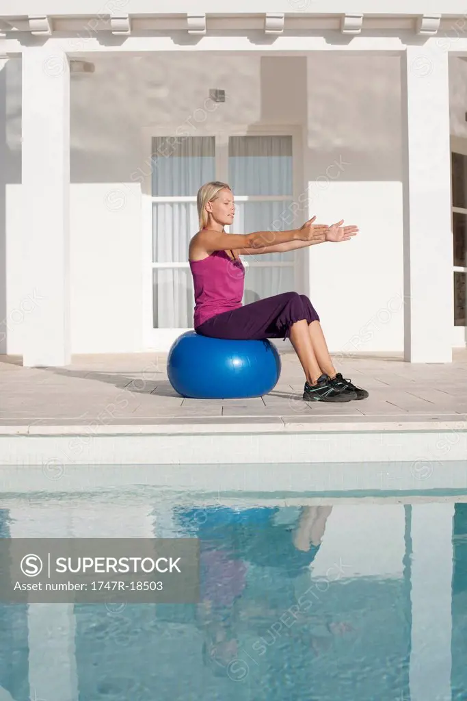 Young woman doing exercise on fitness ball at poolside