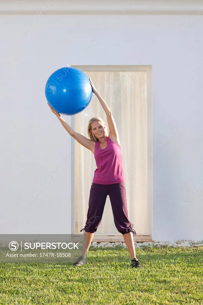 Young woman holding up fitness ball, leaning to one side