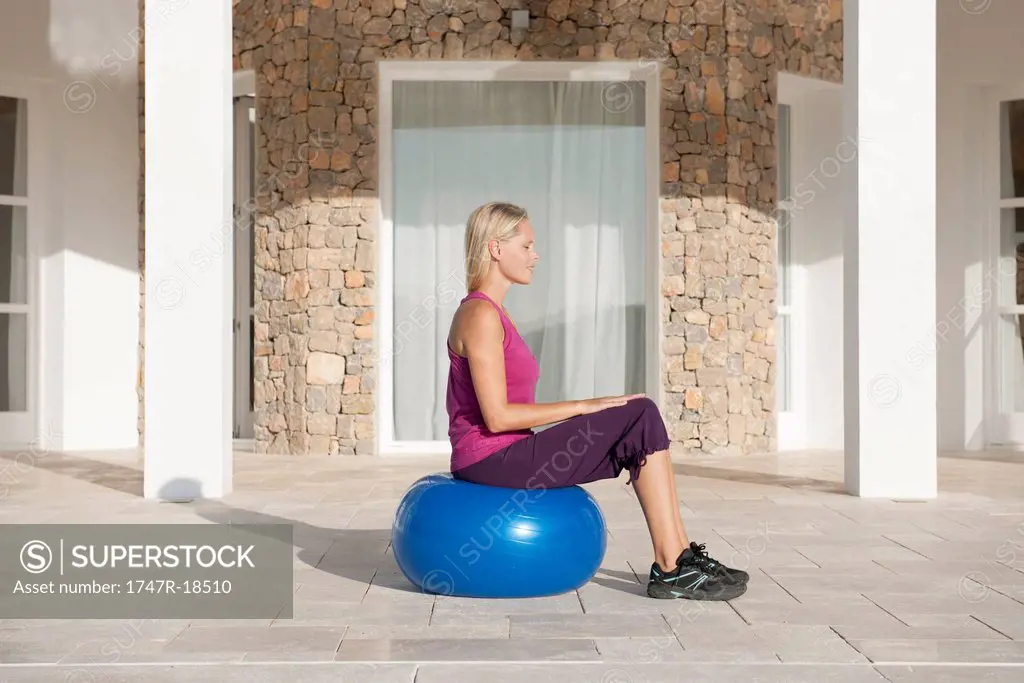 Young woman sitting on fitness ball with eyes closed