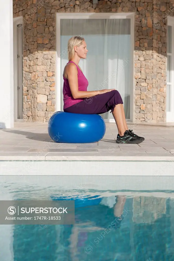 Young woman sitting on fitness ball at poolside