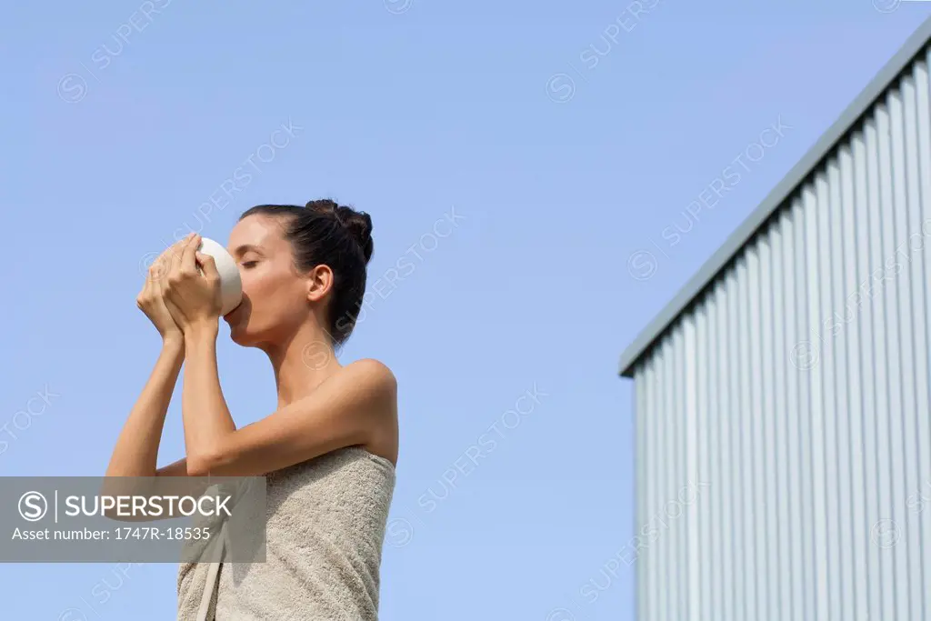 Mid_adult woman wrapped in towel drinking from bowl, side view