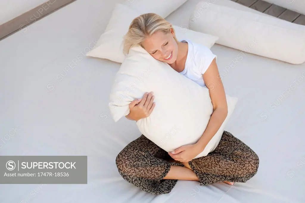 Young woman hugging pillow on bed, high angle view