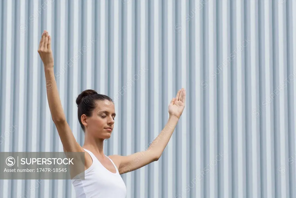 Mid_adult woman meditating outdoors with eyes closed and arms raised