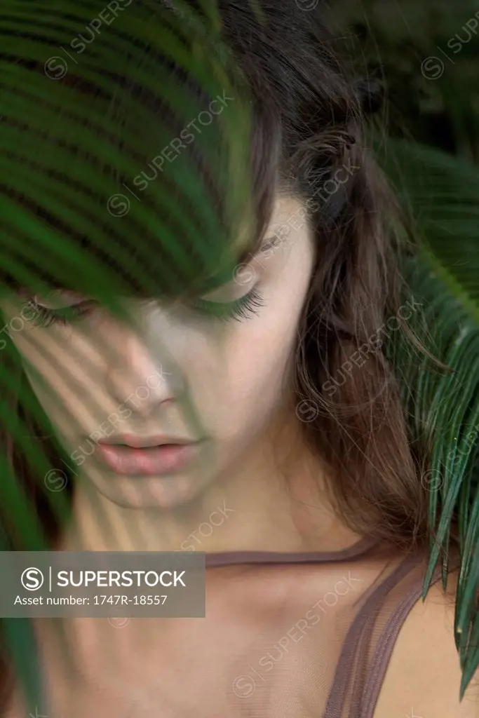 Young woman behind palm frond, looking down sadly