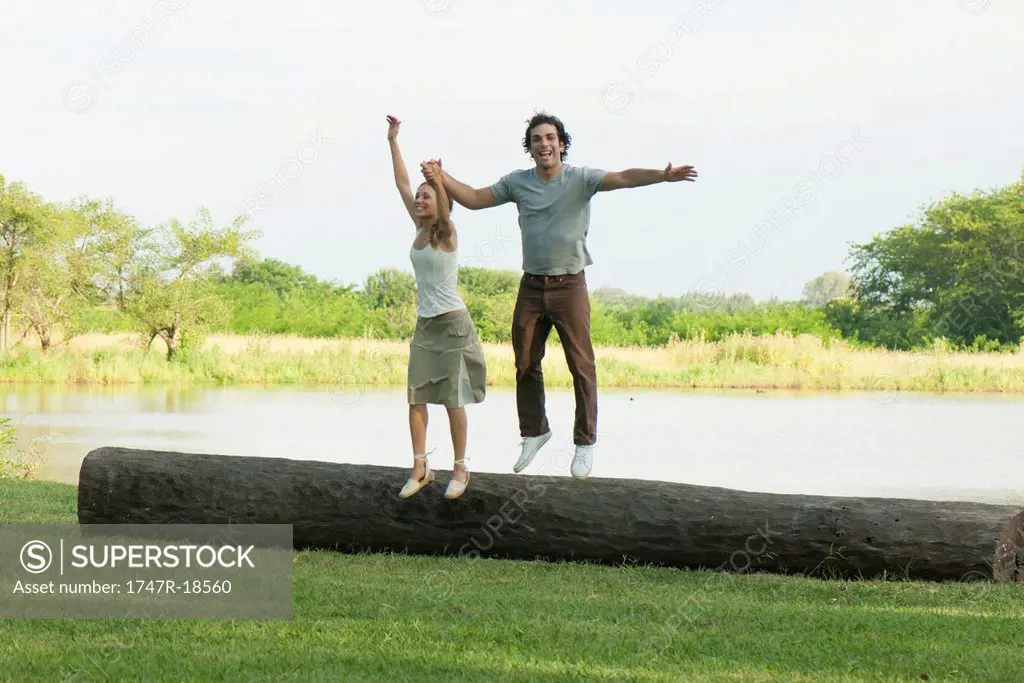 Young couple jumping off log in park