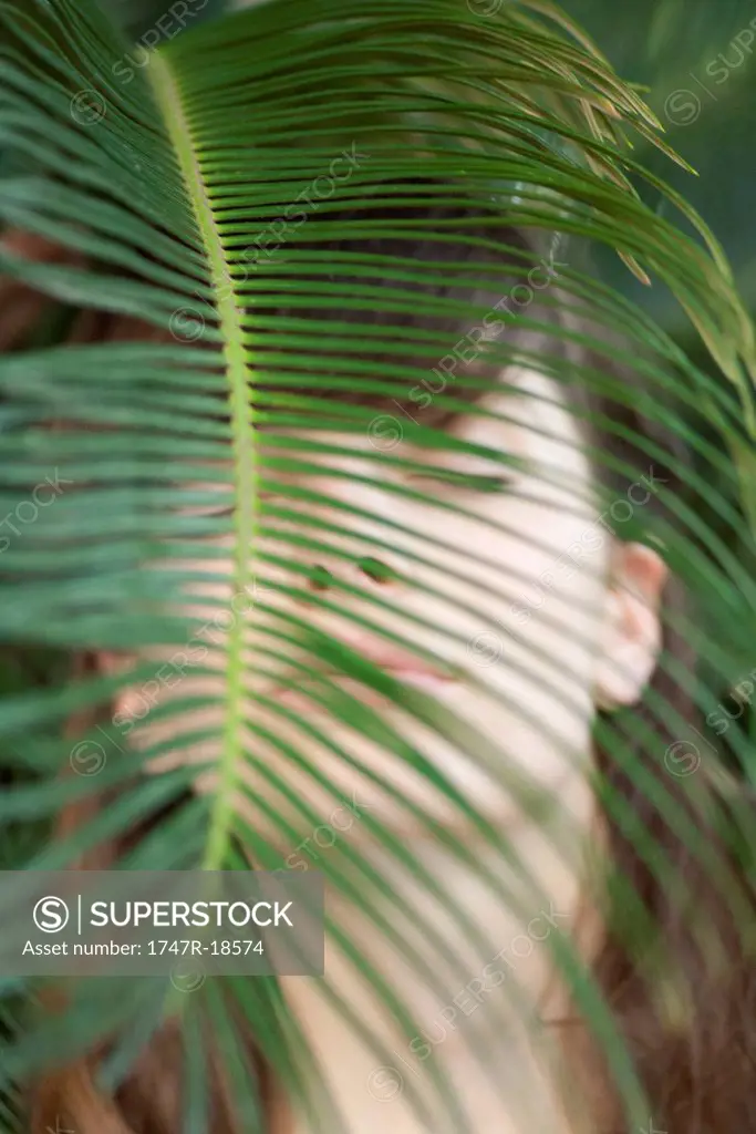 Young woman behind palm frond, eyes closed