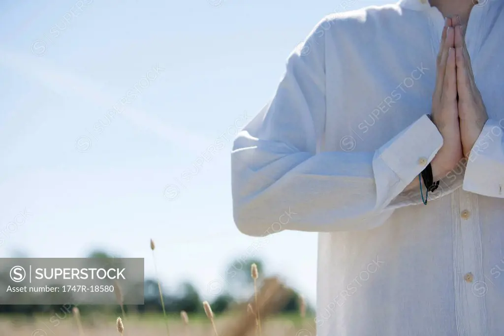 Man outdoors with hands clasped in prayer, cropped