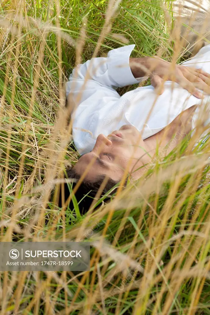 Man lying in tall grass with eyes closed