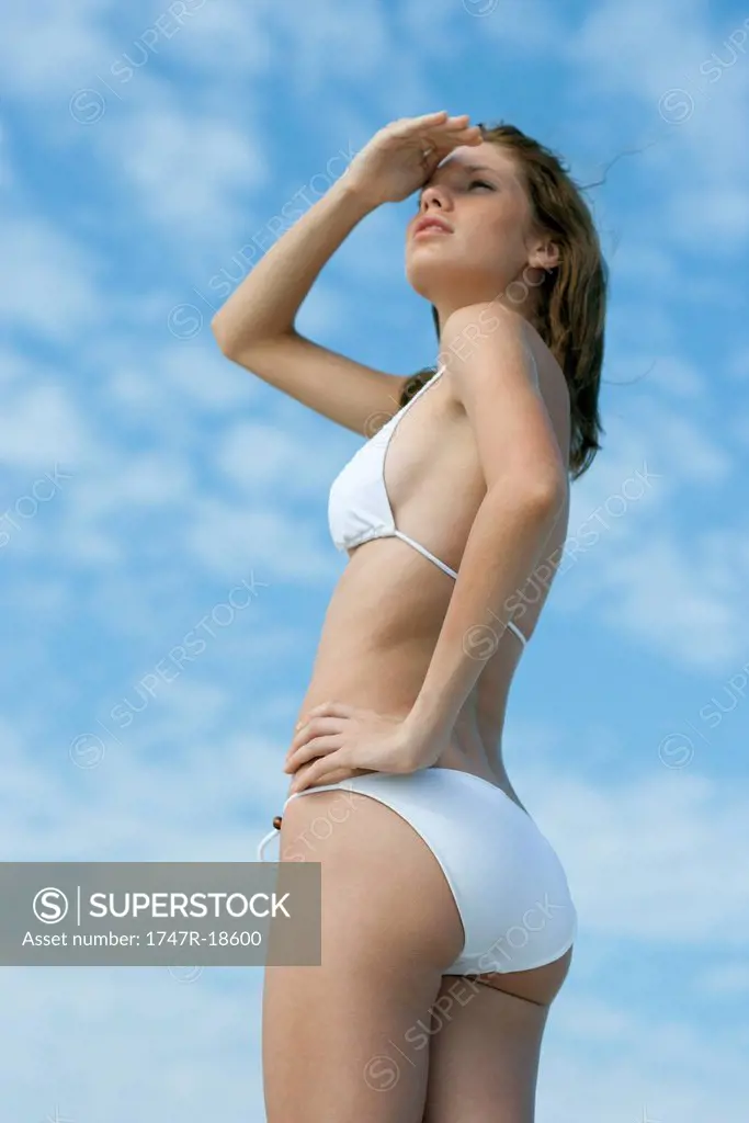 Young woman in bikini looking away, shading eyes