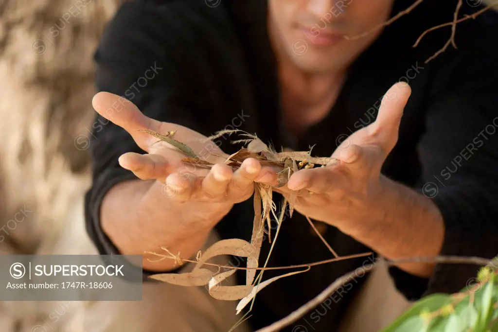 Man holding handful of twigs and leaves, cropped