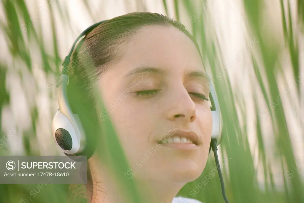 Young woman listening to headphones outdoors with eyes closed