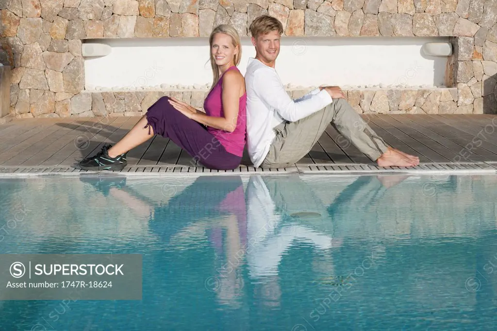 Young couple sitting back to back at poolside, portrait
