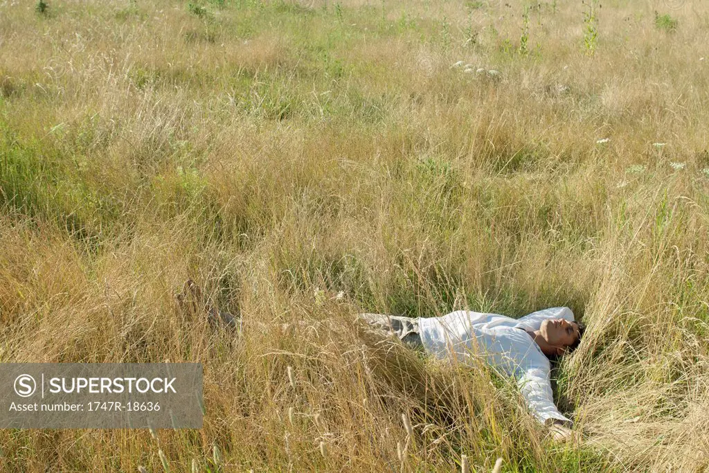 Mid_adult man relaxing in field with eyes closed