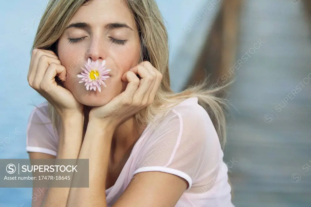 Young woman holding flower in mouth with eyes closed
