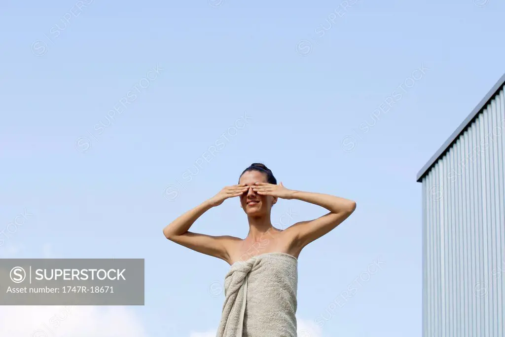 Woman wrapped in towel with hands covering eyes